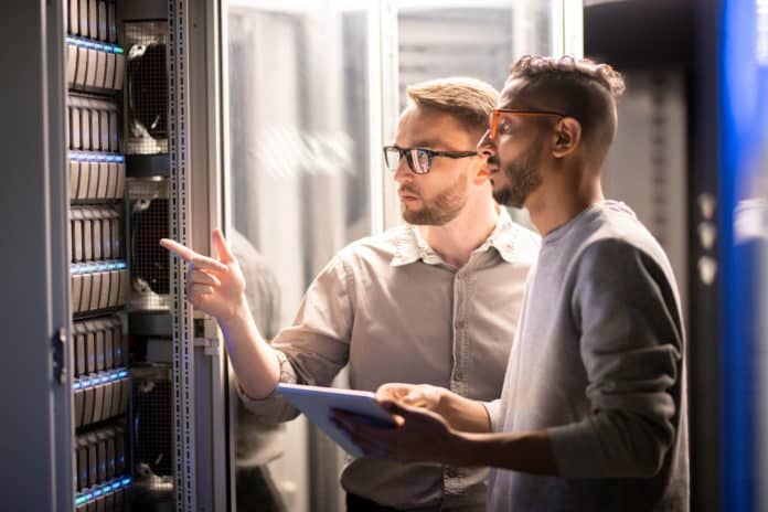 A pair of IT pros review a server in a data center.