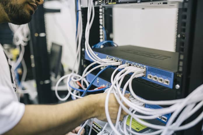 An employees connects a cable to a networking switch.